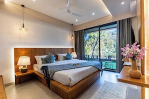 A modern bedroom with a large bed, bedside lamps, a ceiling fan, and a view of the outdoors. - ALAYA STAYS Lakefront Suite Naukuchiatal (Siloti Pant)