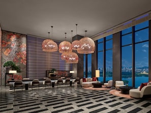 Un moderno vestíbulo de hotel con un amplio espacio de descanso, una pared decorativa y vistas a un paisaje urbano a través de grandes ventanales.