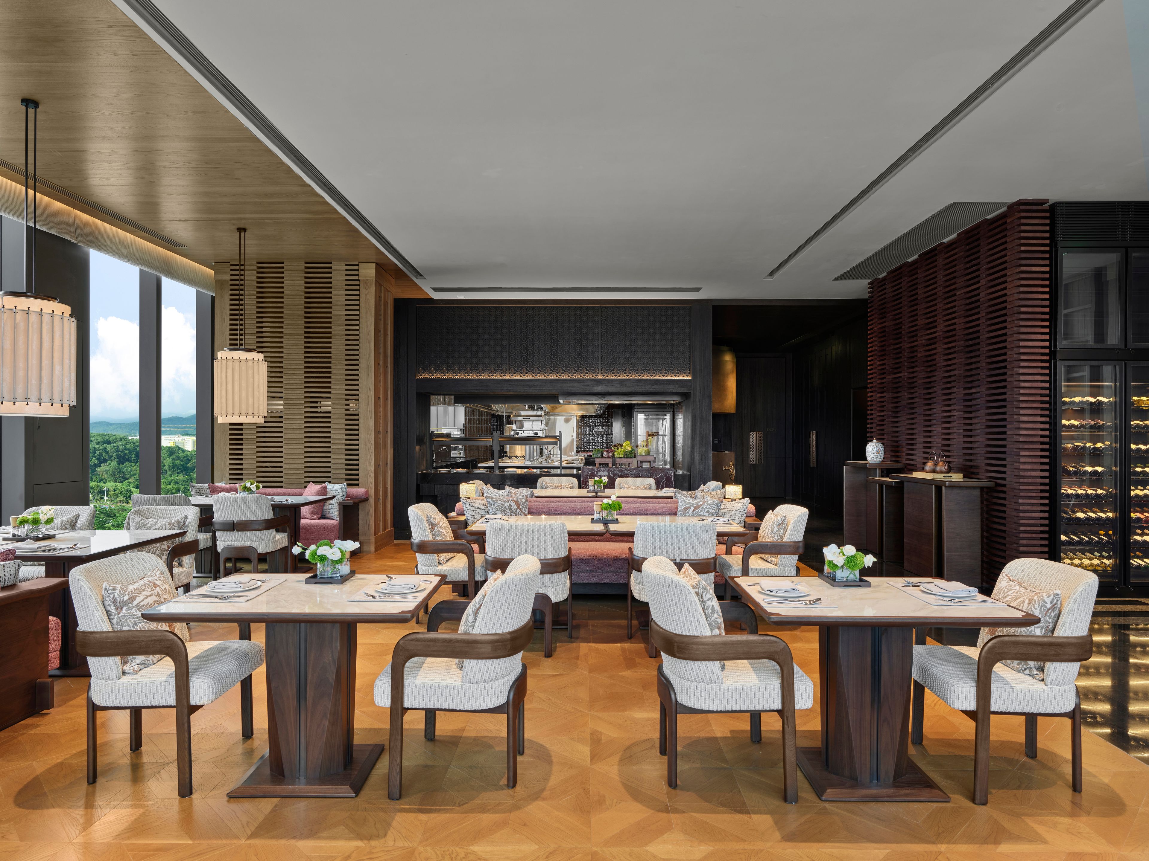 Un comedor moderno con varias mesas y sillas, una barra central, y ventanas amplias con vistas al exterior.