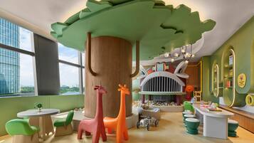 Zona infantil con una gran estructura de árbol, coloridas figuras de animales y una casita.