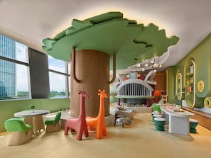Zona infantil con una gran estructura de árbol, coloridas figuras de animales y una casita.