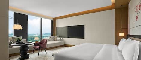 Quarto de hotel moderno com uma cama grande, um sofá, uma mesa de jantar e vista para a cidade.