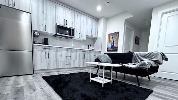 A modern kitchen with grey cabinets, a microwave, and a black rug. - The Suite Spot (Airdrie)
