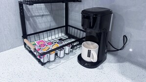A coffee maker, a black wire basket with yogurt containers, and a white mug on a countertop. - The Suite Spot (Airdrie)