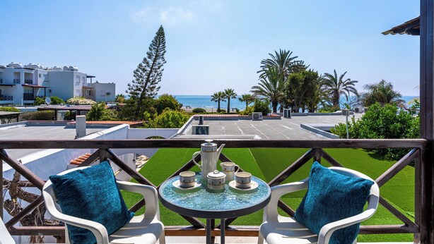 A balcony with a table set for tea, overlooking a beach and palm trees. - Seawaves 1- BR Apt. by Meneou Beach (Meneou)