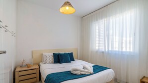 A hotel room with a bed, bedside table, and a hanging light fixture. - Seawaves 1- BR Apt. by Meneou Beach (Meneou)