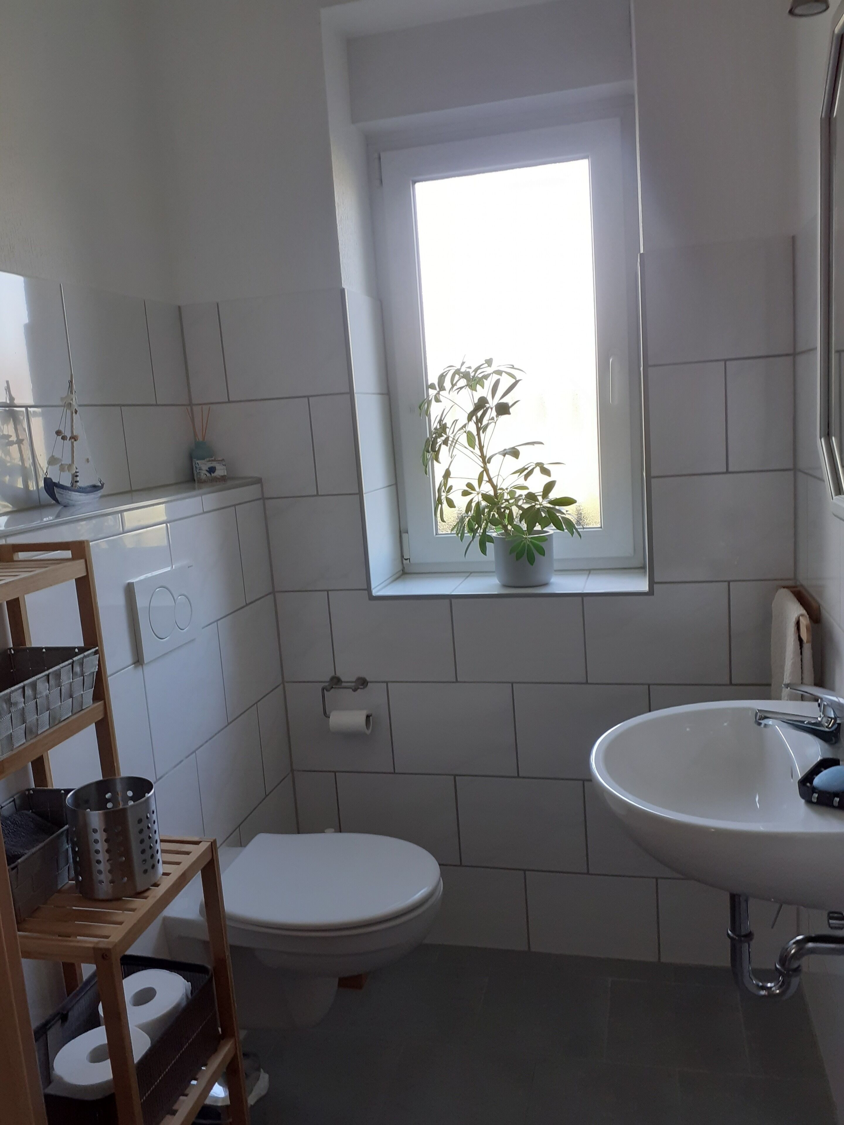 A compact bathroom with a toilet, sink, and a window with a plant.
