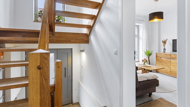 Un intérieur moderne avec un escalier en bois, un coin repas comprenant un canapé et une table, et un espace cuisine avec des meubles en bois.