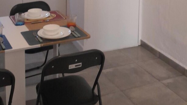 Una cucina compatta con mobili bianchi, un tavolo da pranzo per due persone e una TV a schermo piatto montata a parete.