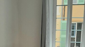 Una stanza con una scrivania bianca, una sedia nera, un portatile, un termosifone e una finestra vista edifici.