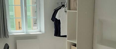 Un dormitorio con cama, armario, silla y ventana con contraventanas.