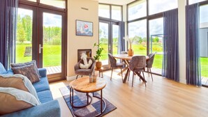 Un amplio salón con sofá, mesa de centro y mesa de comedor con sillas. Una ventana grande ofrece vistas al exterior.
