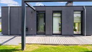 Ein modernes Gebäude mit flachem Dach, großen Fenstern und einer Holzterrasse.