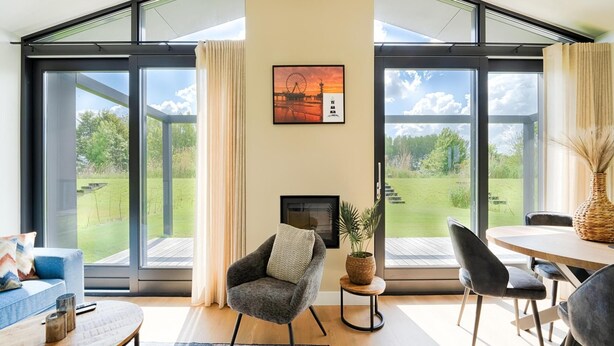 Ein modernes Wohnzimmer mit Kamin, großen Fenstern, einem Essbereich und Blick auf einen Garten.
