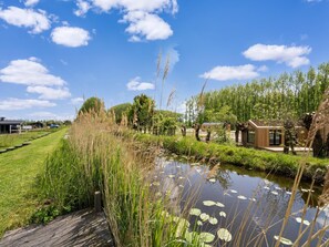 A riverside view with a wooden deck, a small wooden structure, and a grassy area. - Charming stay in Oud Ade by the Kaag (Oud Ade)