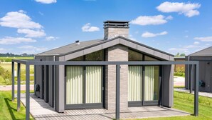 Ein modernes Haus mit überdachter Terrasse, Schornstein und Blick auf die umliegende Landschaft.
