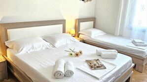 Camera d'albergo con due letti, testiere in legno, biancheria bianca, un comodino con una lampada e decorazioni a parete.
