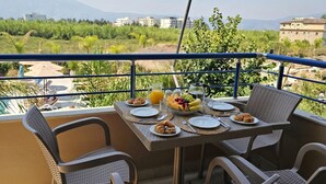 Un tavolo da balcone con prodotti per la colazione, sedie in vimini e vista su spazi verdi ed edifici.