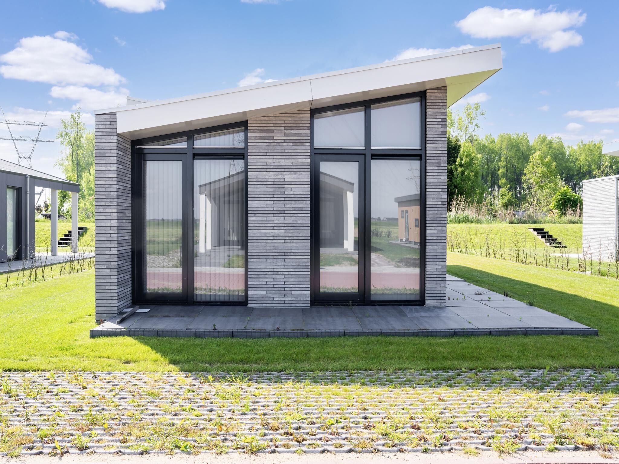 A modern house with large glass windows, a flat roof, and a paved lawn.
