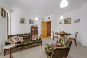 Een woonkamer met een groene bank, een houten bijzettafeltje en een eethoek met een houten tafel en stoelen.
