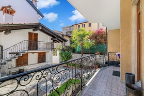 Ein Balkon mit schmiedeeisernem Geländer, eine kleine Gartenanlage mit einer Palme und Blick auf benachbarte Gebäude.