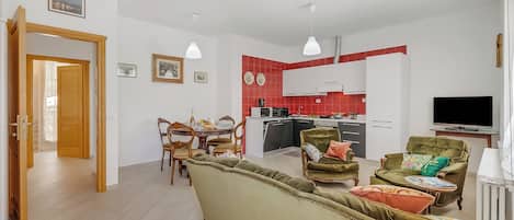 A modern living room with a sofa, chairs, a dining table, and a kitchen area with red tiles.