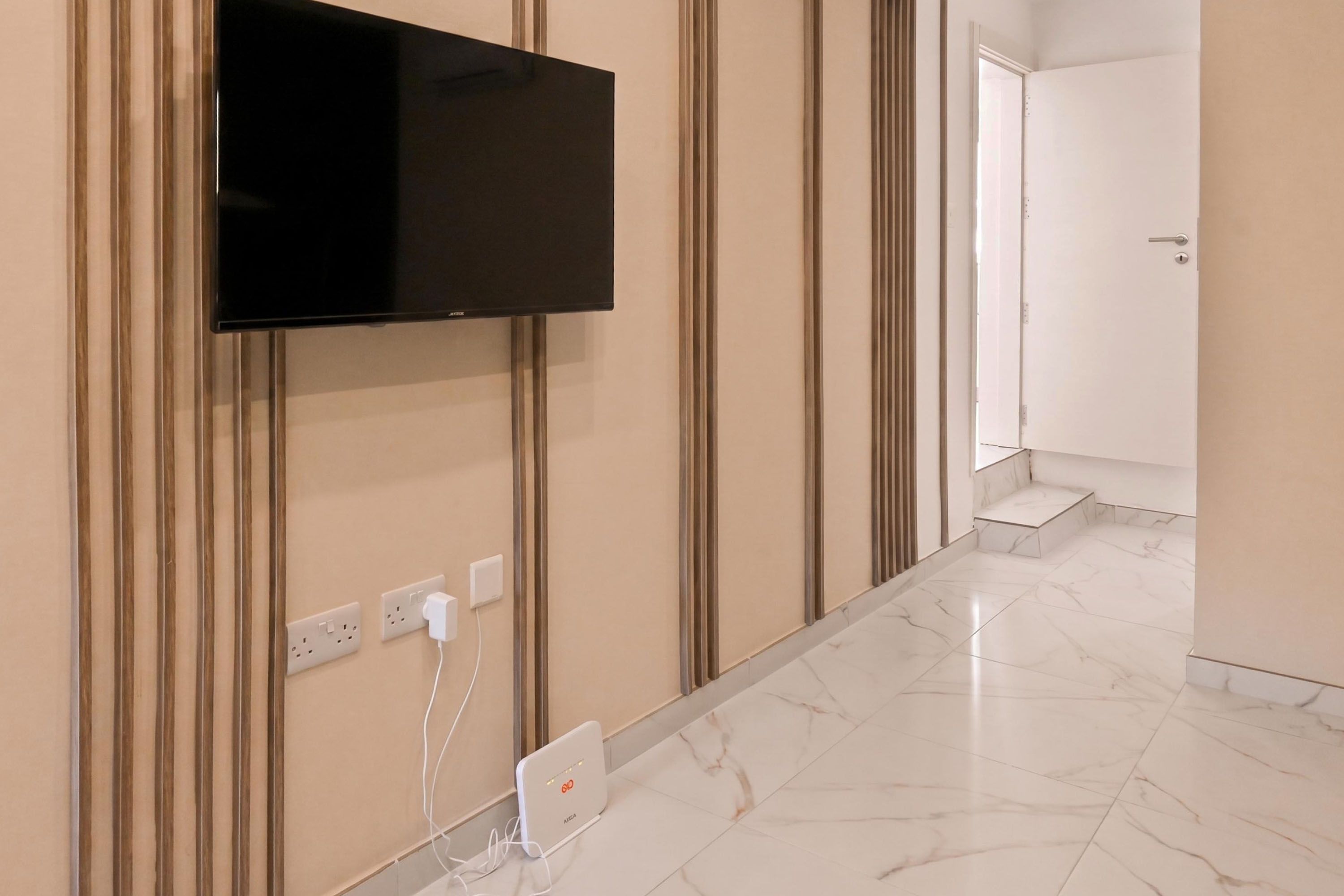 Een moderne hotelkamer met een wandgemonteerde flatscreen televisie, een stopcontact en een oplaadstation op de vloer.