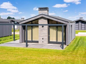 Une maison moderne dotée d’un patio couvert, d’une cheminée et d’une pelouse bien entretenue.