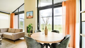 Un salon moderne avec un canapé, une table à manger et des chaises, une plante en pot et un tableau accroché au mur.