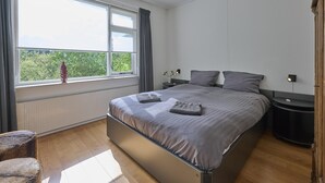 A bedroom with a large bed, two bedside tables, a window with curtains, and a radiator. - Rural holiday home with expansive views (Aalten)