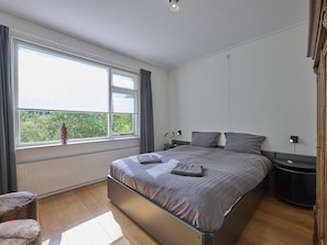 A bedroom with a large bed, two bedside tables, a window with curtains, and a radiator. - Rural holiday home with expansive views (Aalten)