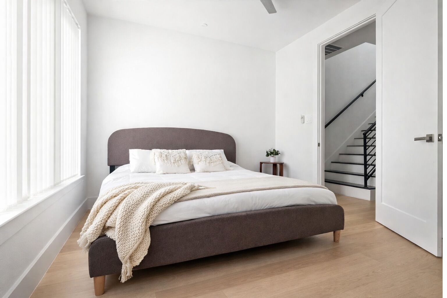 Una camera da letto moderna con un letto grande, un comodino con una pianta e una scala che conduce a un piano superiore.