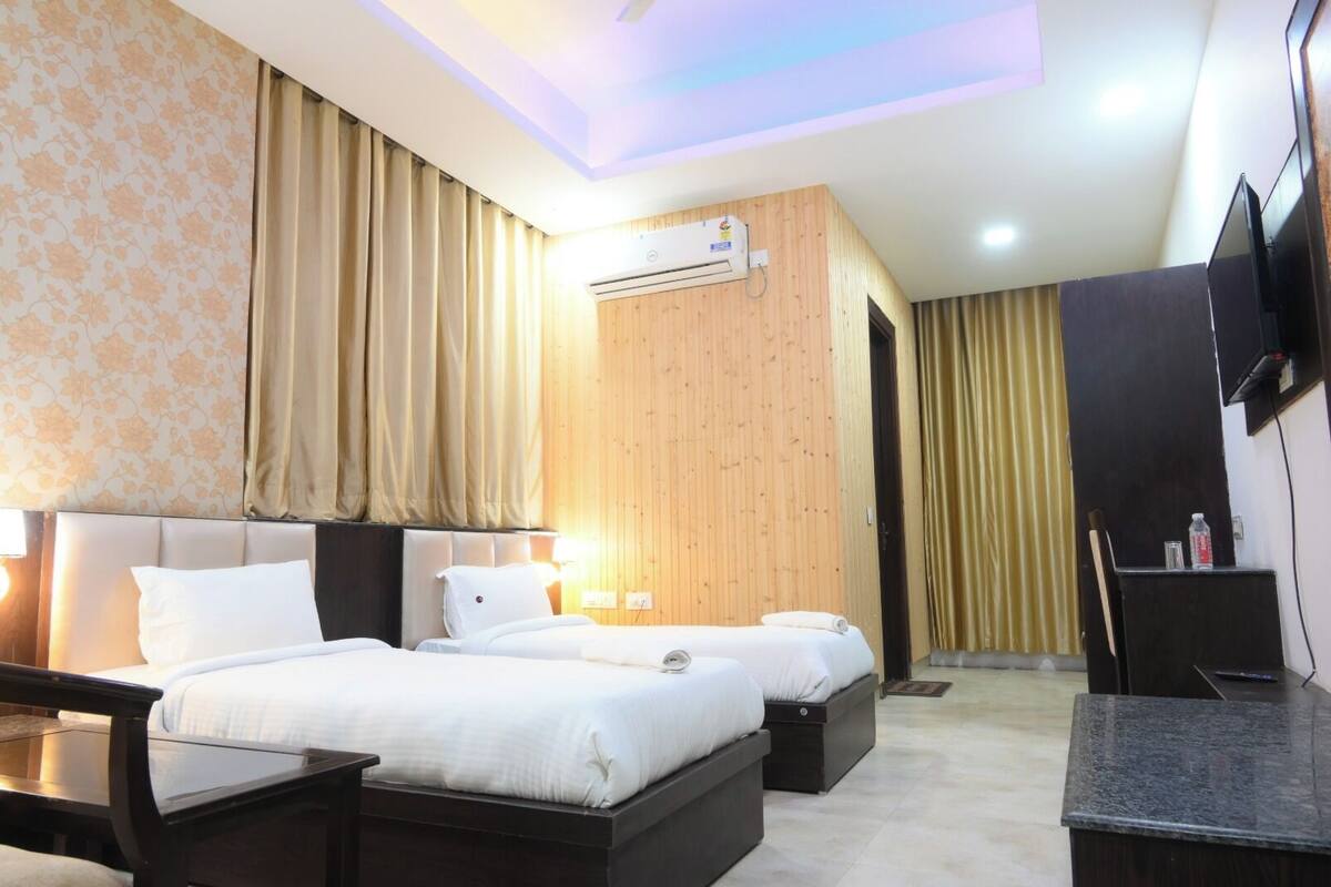 A hotel room with two beds, a flat-screen TV, a wooden accent wall, and an air conditioning unit.
