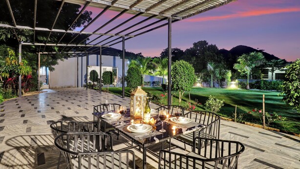Ein Essbereich im Freien mit einer überdachten Pergola, einem gedeckten Tisch und Blick auf einen angelegten Garten und sanfte Hügel.