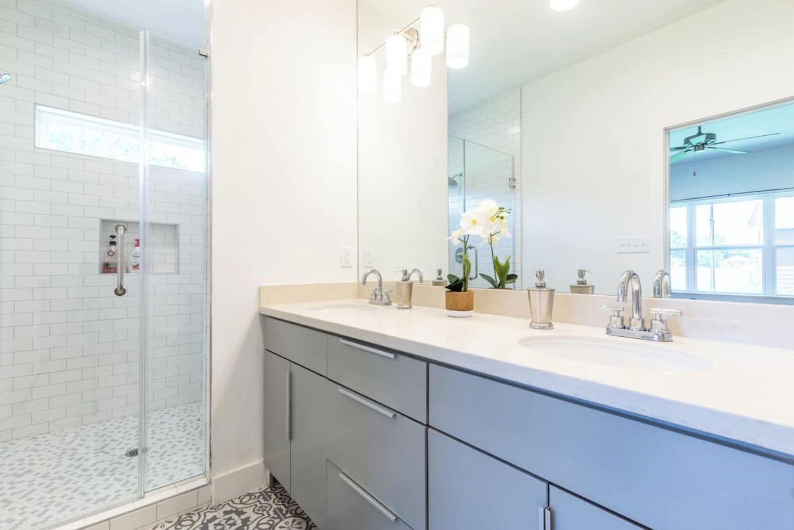 Une salle de bain moderne avec une douche à parois de verre, un grand miroir et un meuble-lavabo doté de deux vasques.