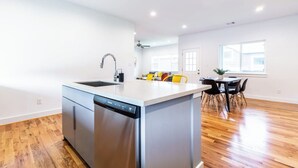 A modern kitchen with a dishwasher, a sink, and a dining area with a table and chairs. - 111 Lavish Bungalow 1753! Medical Center, Stadiums (Houston)