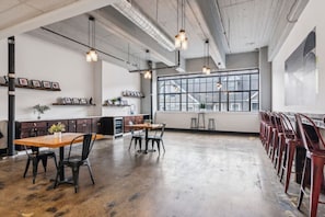 A spacious dining area with high ceilings, exposed ductwork, and pendant lighting. Tables and chairs are arranged for dining. - Chic Loft | Free Parking, Gym, Game Room (Philadelphia)