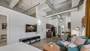 Un espace de vie moderne comprenant un téléviseur à écran plat, un canapé, une table à manger et un coin cuisine.