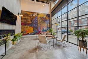 A spacious lobby with a large mural, comfortable seating, and large windows offering a view of the outside. - Chic Loft | Free Parking, Gym, Game Room (Philadelphia)
