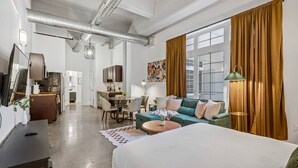 Une chambre d’hôtel moderne avec un grand lit, un canapé, un coin repas et une cuisine en arrière-plan.