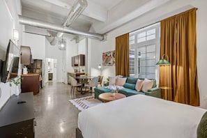 A modern hotel room with a large bed, a sofa, a dining area, and a kitchen in the background. - Chic Loft | Free Parking, Gym, Game Room (Philadelphia)