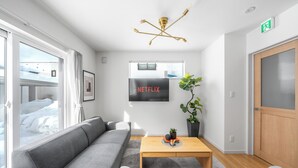 A modern living room with a grey sofa, a wooden coffee table, a plant, and a wall-mounted TV labeled 'NETFLIX.' - BEAR CUB HOTEL (Asahikawa)