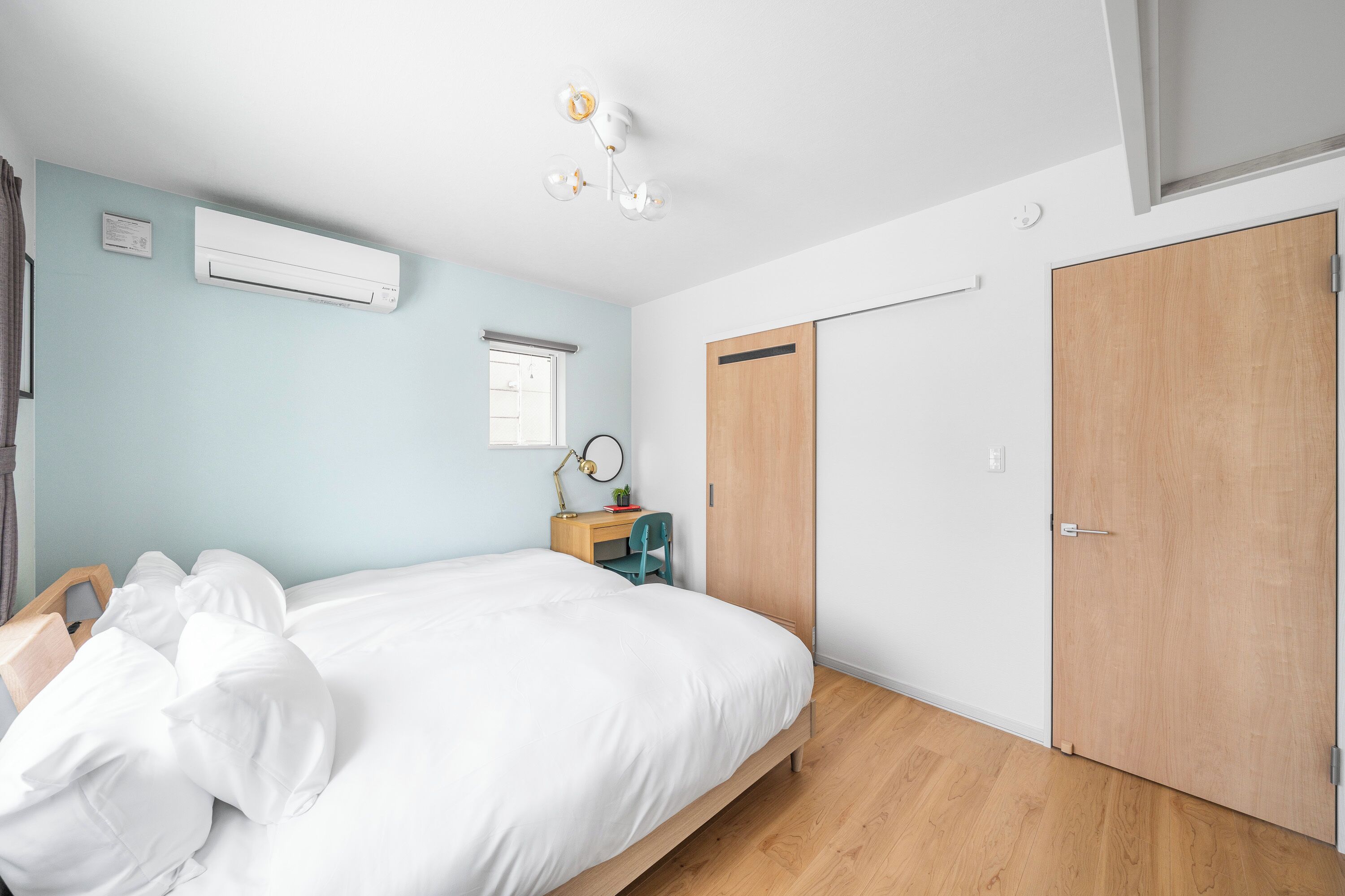 A bedroom with a bed, a desk, an air conditioner, and a wardrobe.