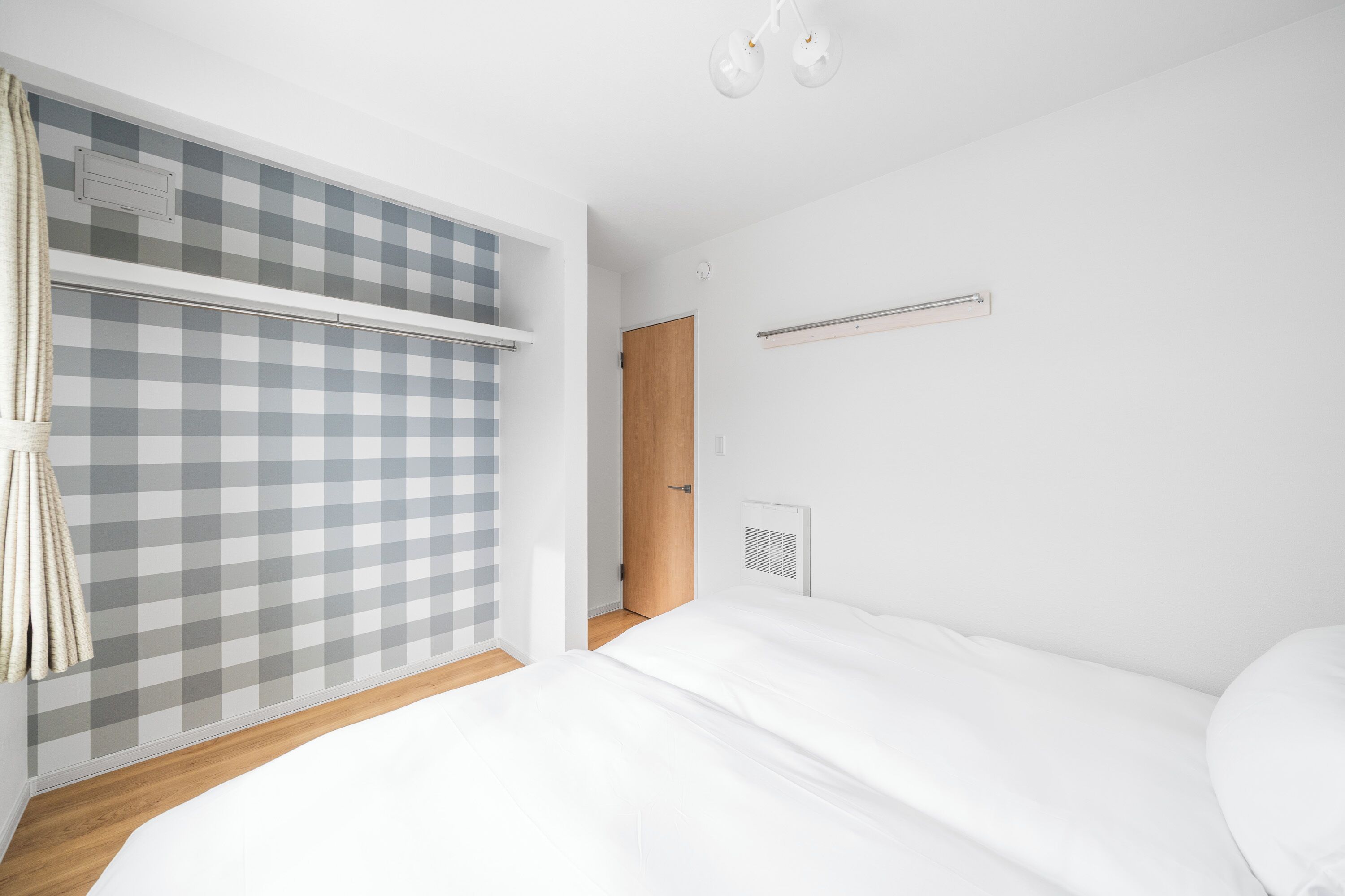 Un dormitorio con una cama, una cortina a cuadros, una puerta de madera y una pared blanca.