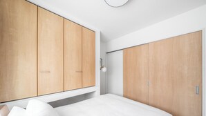 A bedroom with a bed, wooden wardrobe, and a bedside table. - BEAR CUB HOTEL (Asahikawa)