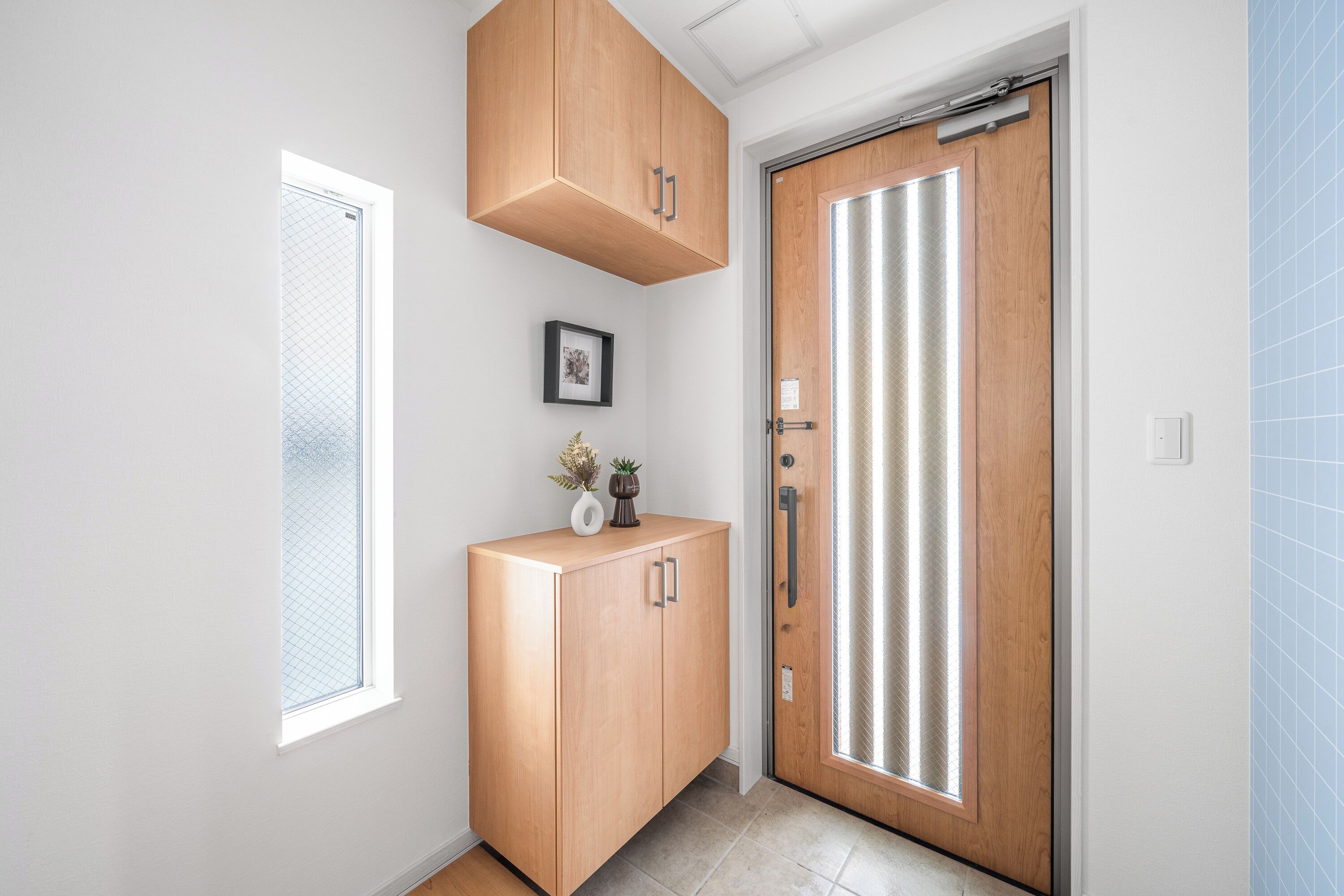 Un couloir avec une armoire en bois, une porte dotée d’un panneau en verre dépoli et un petit tableau encadré accroché au mur.