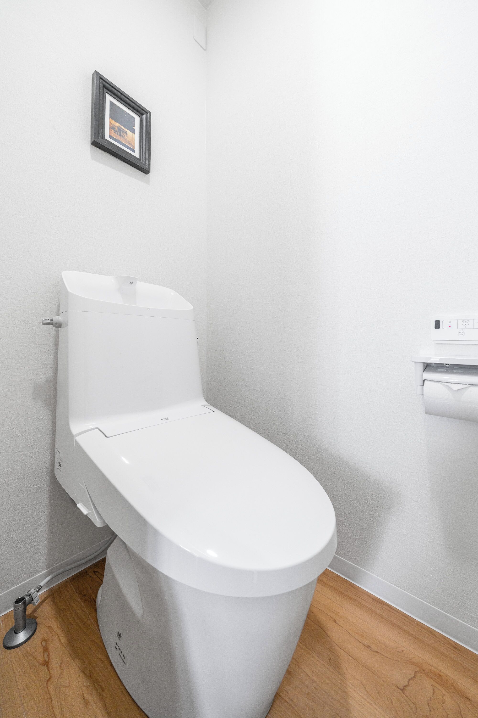 A modern bathroom with a white toilet, a framed picture on the wall, and a paper towel dispenser.