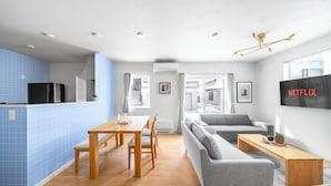 A modern living space with a dining area, sofa, and a TV mounted on the wall. - BEAR CUB HOTEL (Asahikawa)