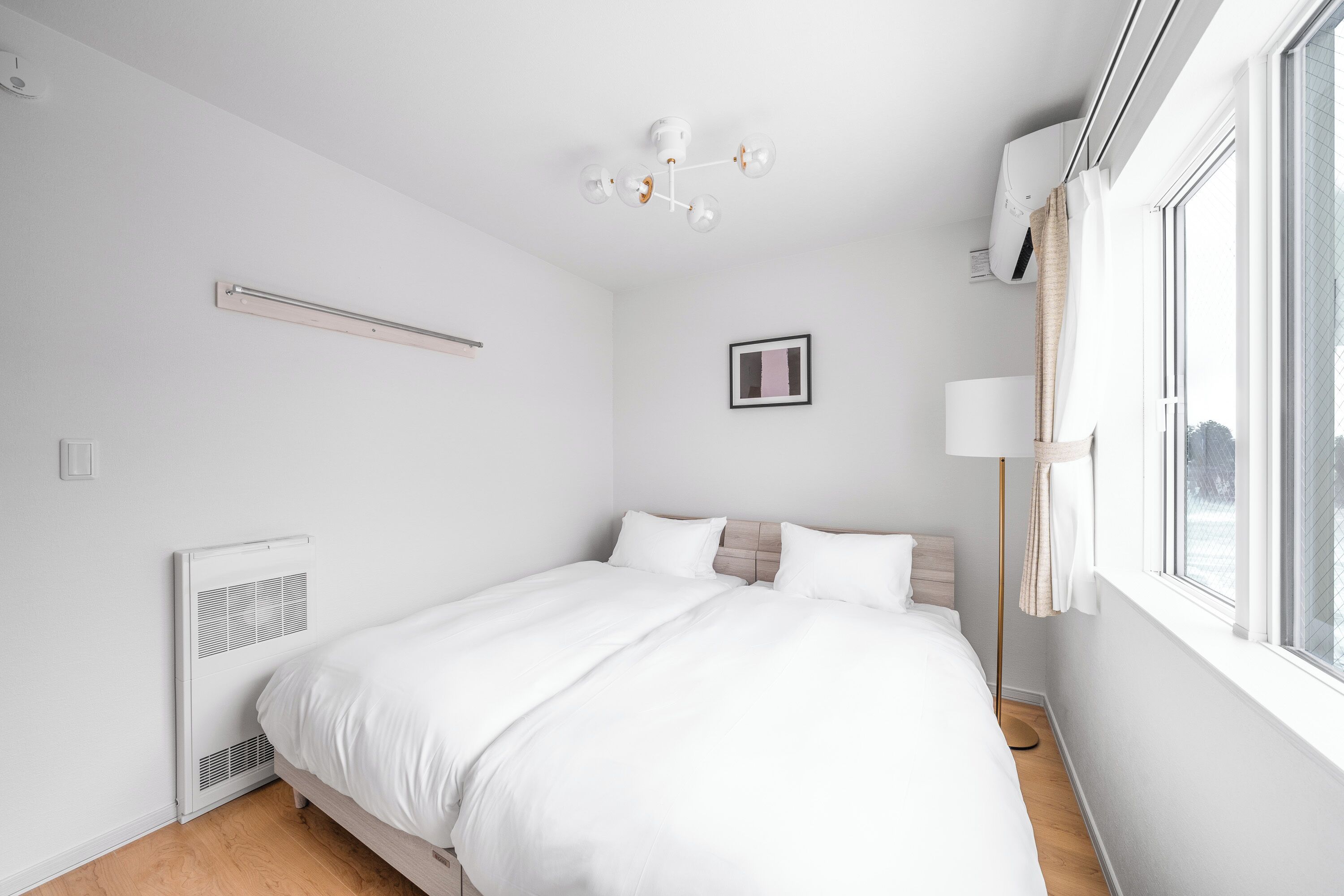 A bedroom with a bed, a ceiling light, a window, and a wall-mounted air conditioner.