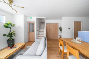 Un interior moderno con sofá, mesa de comedor de madera, escalera y una planta en maceta.